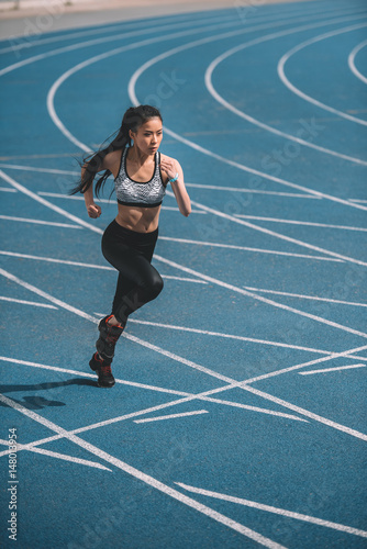 Athletic young sportswoman sprinting on running track stadium