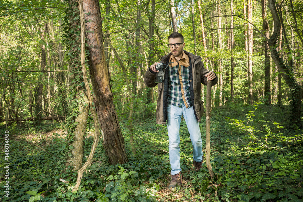 Young man is taking photo with his retro camera while hiking in the woods Young man is taking photo with his retro camera while hiking in the woods