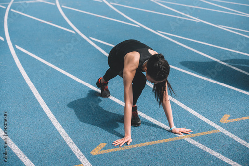 Concentrated young sportswoman in starting position on running track stadium