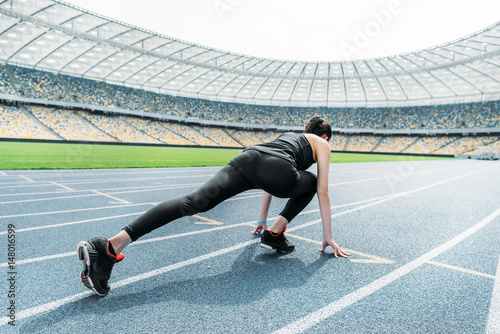 Young fitness woman in sportswear in starting position on stadium