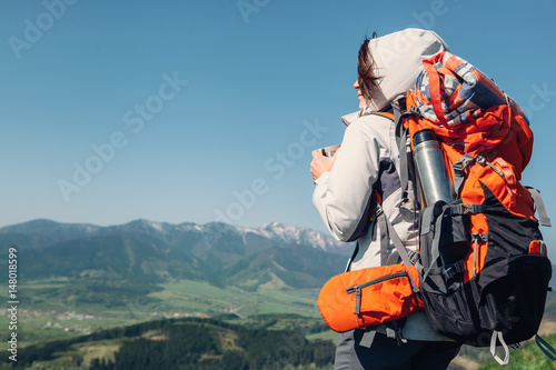 Woman backpacker traveler drinks hot tea on the mountain top