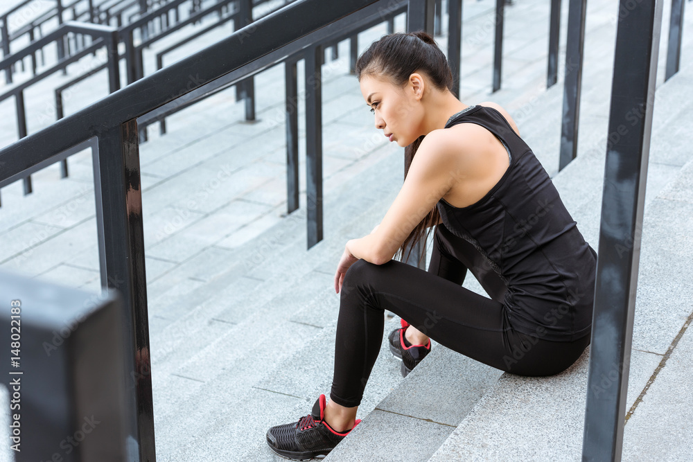 Young tired sportswoman in sportswear sitting on stadium stairs Young tired sportswoman in sportswear sitting on stadium stairs