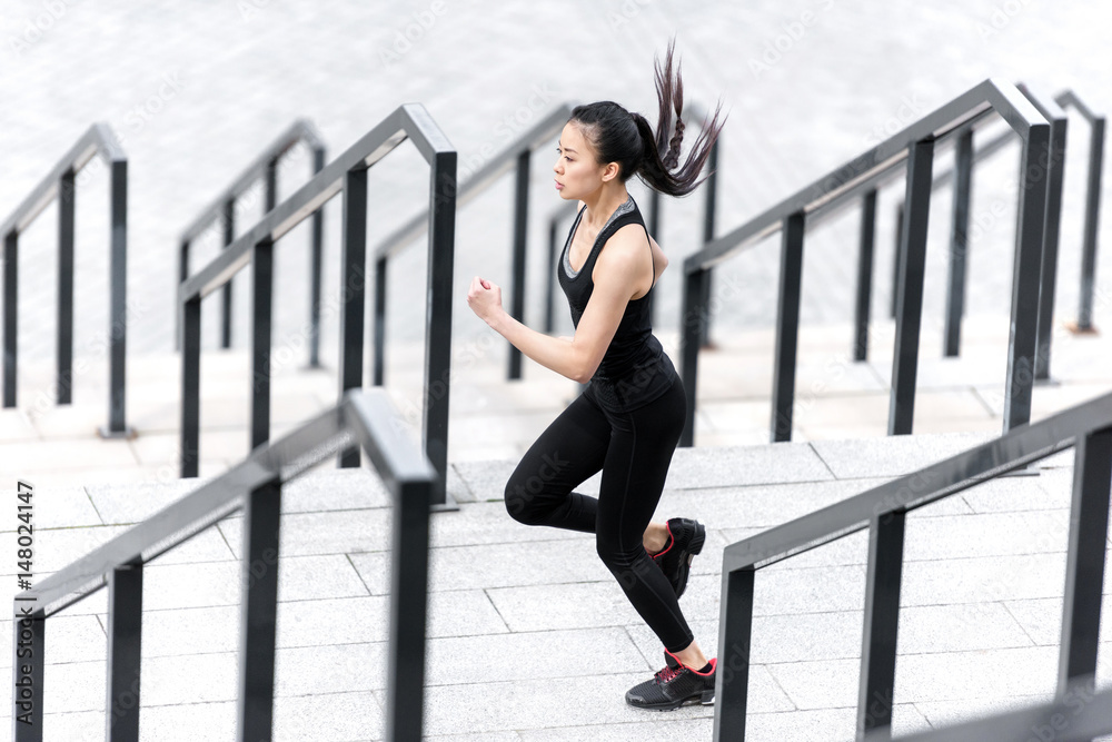 Side view of athletic young woman in sportswear running on stadium stairs
