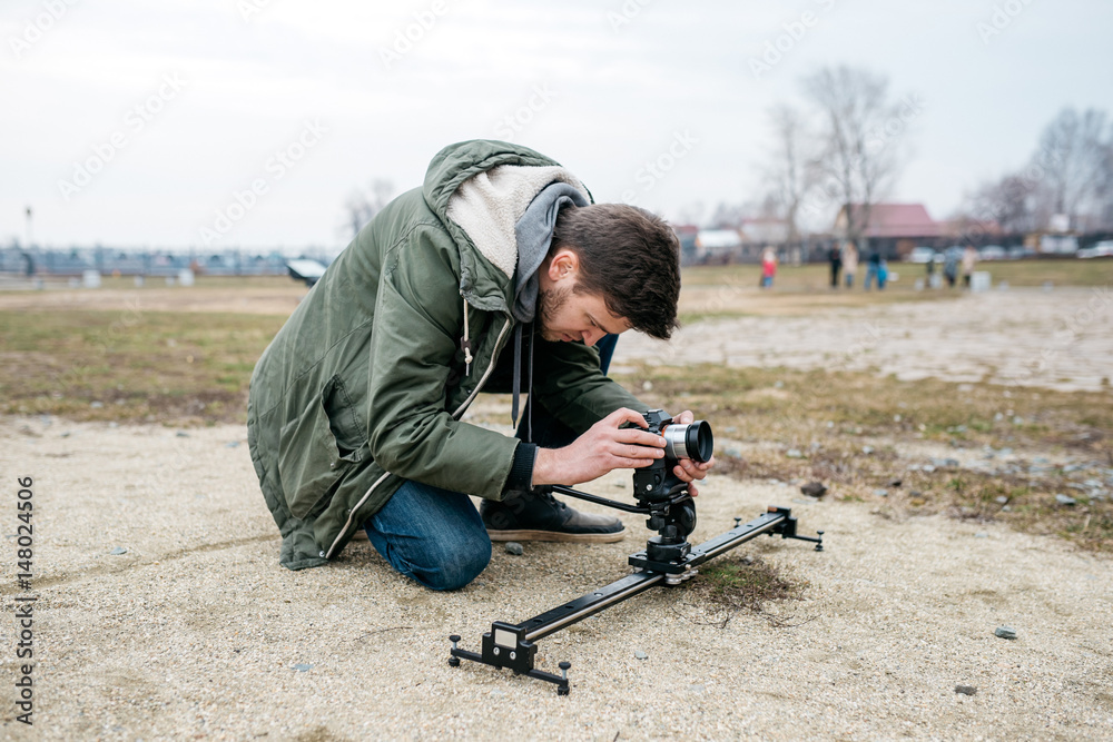 Obraz premium The cameraman shoots on the camera, outdoors. Sits on his knees and look into the lens