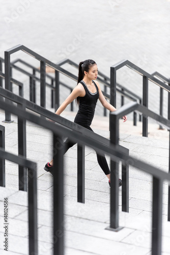 Young sporty asian woman in sportswear jogging on stadium stairs