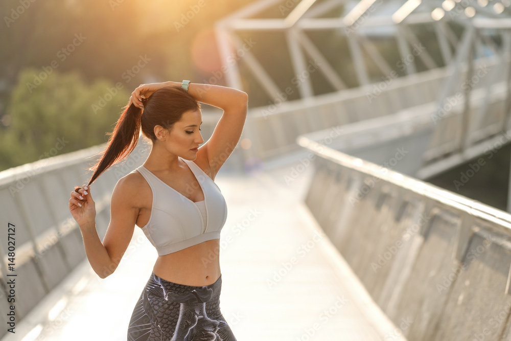 Beautiful fit woman ready for an outdoor urban fitness workout. Long hair brunette model lacing ponytail before training.