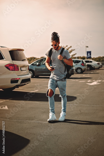 Man with dreadlocks using phone on a parking lot