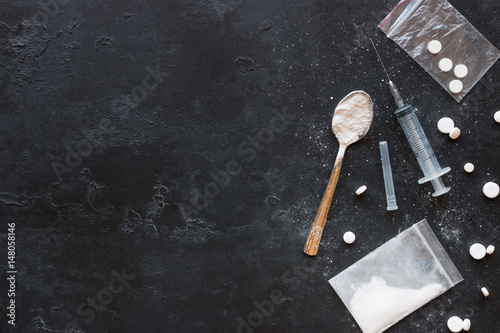 Drugs in the form of powder and tablets, a spoon and a syringe on a black background mockup photo