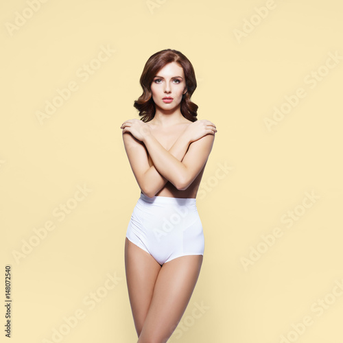 Beautiful, sexy, young girl posing topless in slim underwear over yellow background. © Acronym
