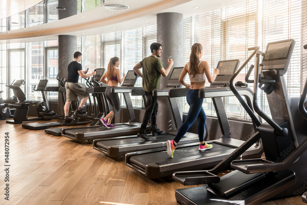 Group of four people running on treadmills in fitness gym