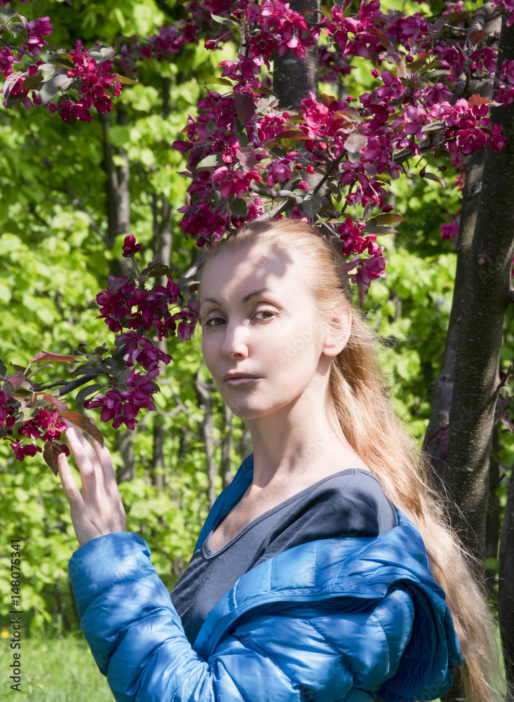 young attractive woman standing near the blossoming crimson apple tree