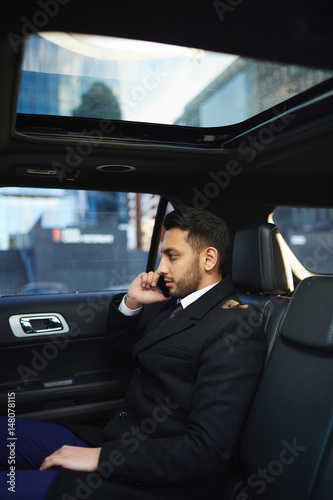 Side view portrait of handsome Middle-Eastern businessman speaking by phone on backseat inside expensive car © pressmaster