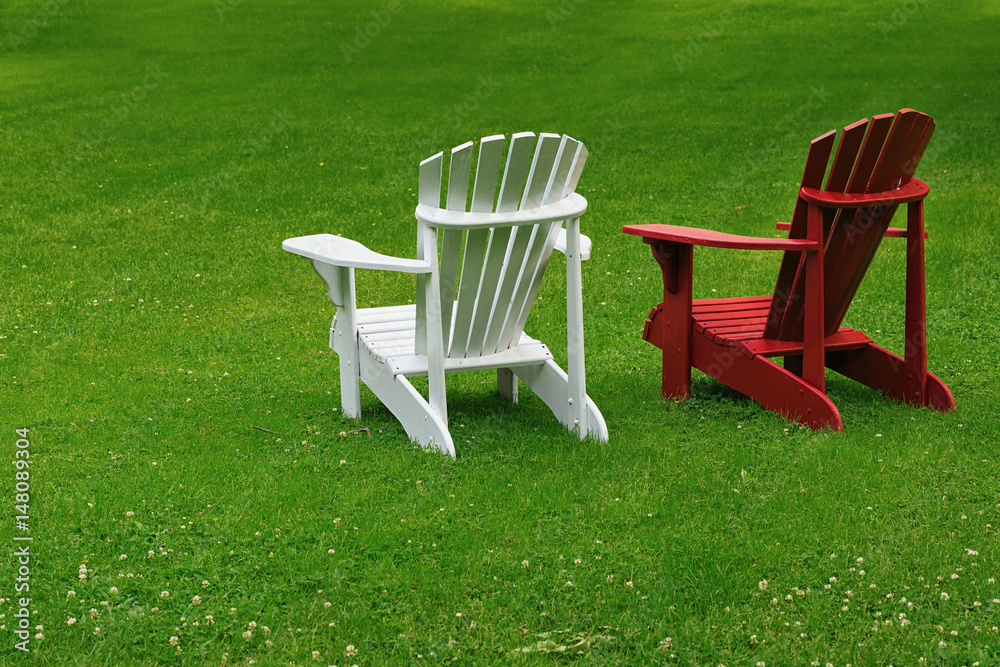 Red and white Adirondack chairs on a extensive lawn. Red and white Adirondack chairs on a extensive lawn.