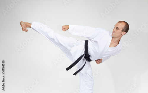 Adult athlete trains a kick on a gray background