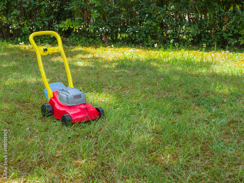 Push lawn mower toy on the grass in a garden . No people