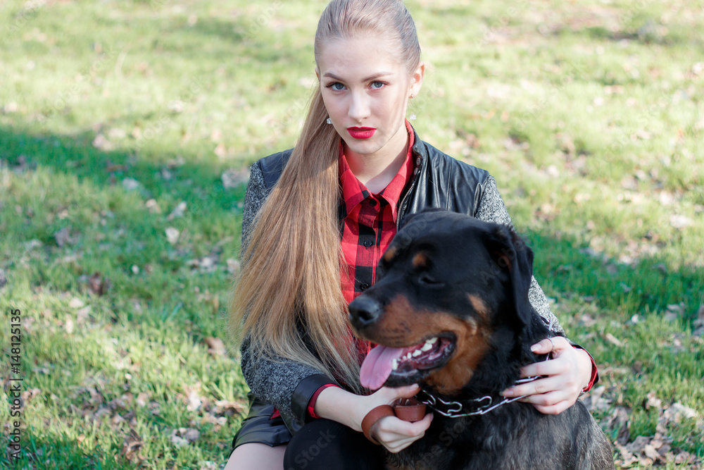 Beautiful blonde crouched down on the grass to her dog, breeds a rottweiler, holds her by the collar Beautiful blonde crouched down on the grass to her dog, breeds a rottweiler, holds her by the collar