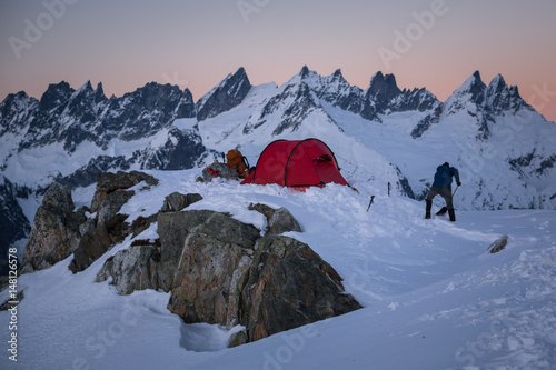 Man shoveling snow at sunset by campsite and mountains, North Cascade, Beckler Peak, Washington, USA photo