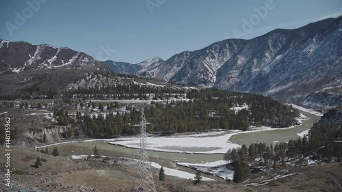 Russia, Siberia, Altai Mountains. beautiful mountain valley in the early spring - snow on the mountain peaks and an ice drift on the river. Mountains and electric power line towers. photo