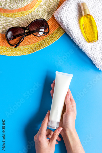 Sun protection composition with glasses and cream on blue background top view