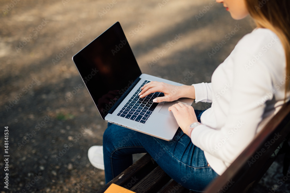 Woman sitting on bench outside and working on computer in park Woman sitting on bench outside and working on computer in park