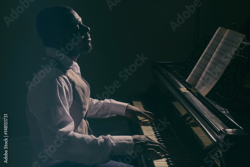 Photography Afro American man playing piano in darkness