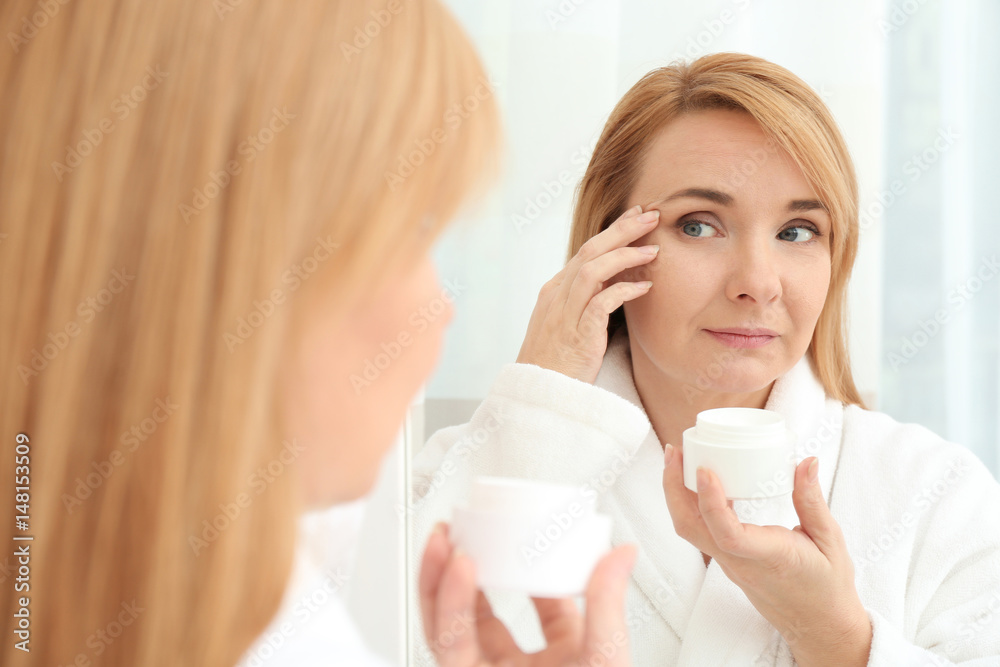 Happy senior woman applying anti-aging cream near mirror Happy senior woman applying anti-aging cream near mirror
