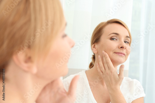 Happy senior woman applying anti-aging cream near mirror