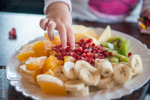 Child's hand takes piece of fruit from plate