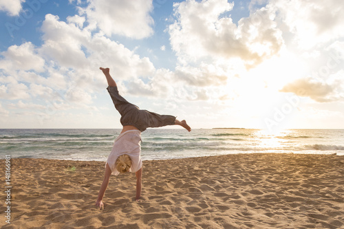 Relaxed woman enjoying sun, freedom and life turning cartwheel on beautiful beach in sunset. Young lady feeling free, relaxed and happy. Vacations, freedom, happiness, enjoyment and well being. photo