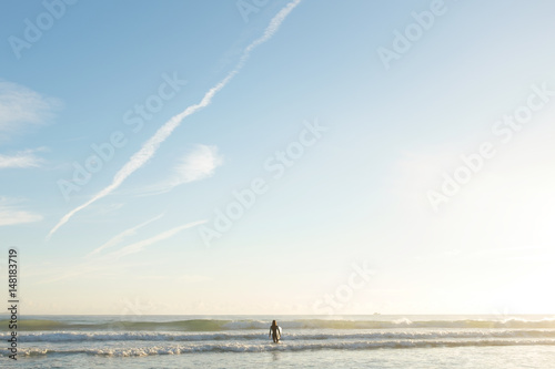 Young female surfer entering the ocean at sunrise, surf paradise