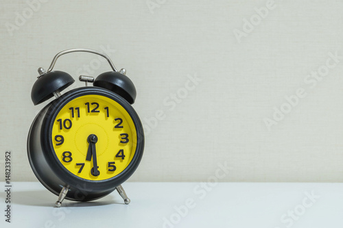 Closeup yellow and black alarm clock for decorate show half past six or 6:30 a.m. on white wood desk and cream wallpaper textured background tone with copy space