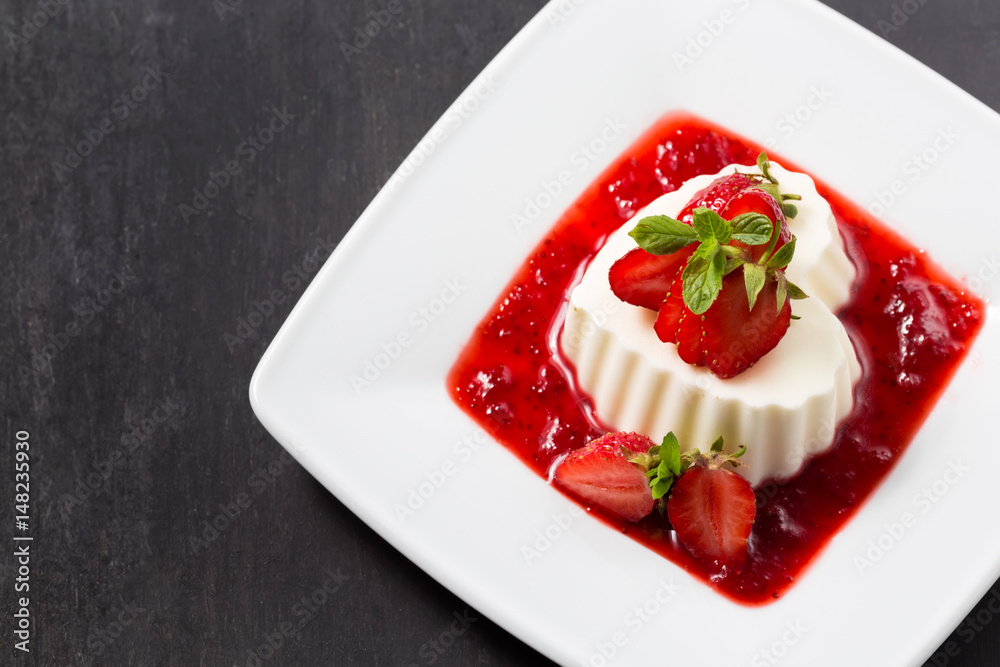 Vanilla panna cotta with strawberry jam on a white plate. Dark background. Valentine's day concept Vanilla panna cotta with strawberry jam on a white plate. Dark background. Valentine's day concept