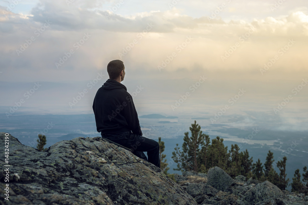 Man is sitting on a stone hillside, hands looking at the view from the heights and enjoys the freedom