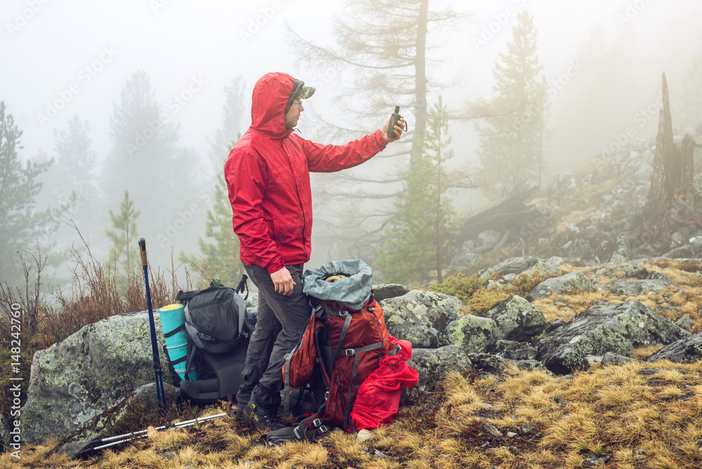 Fototapeta premium Hiker travels in the mountain forest in the mist with a backpack and trying to find a mobile connection
