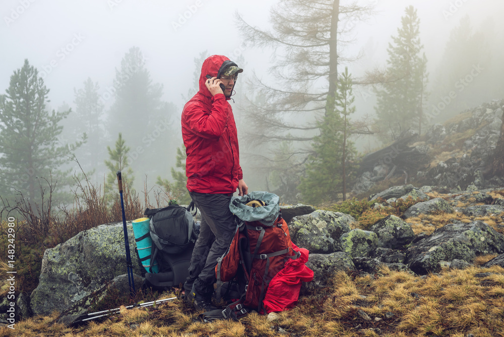 Fototapeta premium Hiker travels in the mountain forest in the mist with a backpack and trying to find a mobile connection