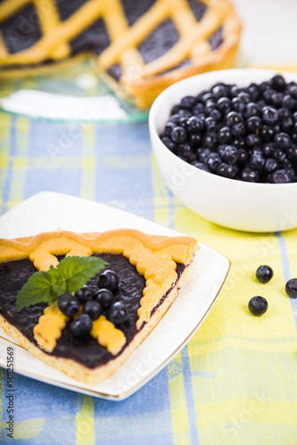 Piece of a blueberry pie and fresh berries on a wooden table.