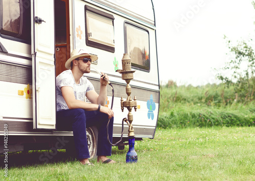 Young, handsome hipster smoking hookah outdoors. Holiday, vacation, trip concept.