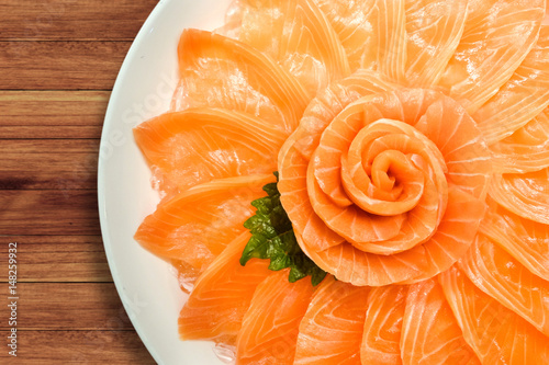 Top view of salmon sashimi serve on flower shape in white ice bowl boat isolated on wood table background, Japanese style.