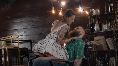 Erotic girl with a dangerous razor in her hands is going to shave her beard to a brutal man who sits on a hairdresser's armchair in a vintage location in Slow motion