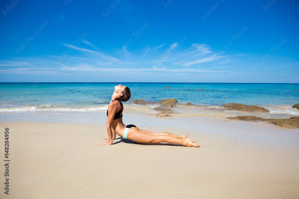 Healthy yoga exercise on the beach, slim sporty body training, leisure and meditation, vacation, sport, health care concept, over natural background blue sky and sea. Cobra pose