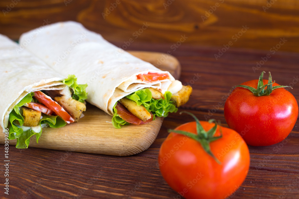 
Kebab with chicken. Shaurma with meat, cabbage, tomato, lettuce leaf, sauce on a wooden background.  