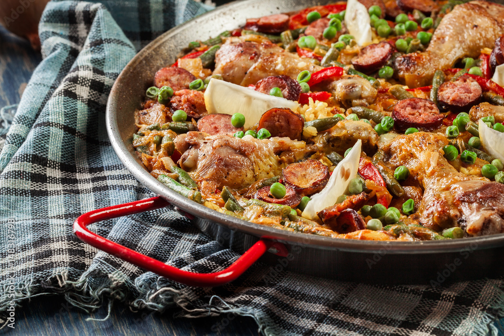 Traditional paella with chicken legs, sausage chorizo and vegetables served in paellera Traditional paella with chicken legs, sausage chorizo and vegetables served in paellera
