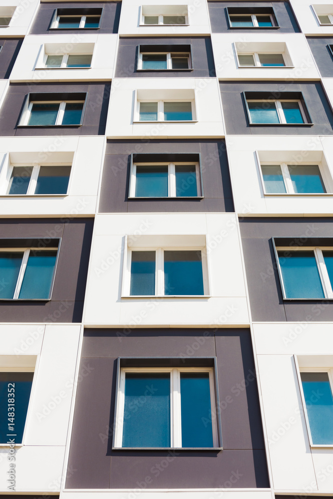 Fototapeta premium From below shot of modern and new apartment building. Photo of a tall block of flats against a blue sky.