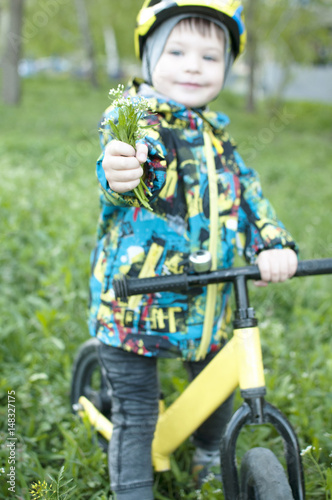 A child holds out a bouquet of flowers, sits on a bicycle