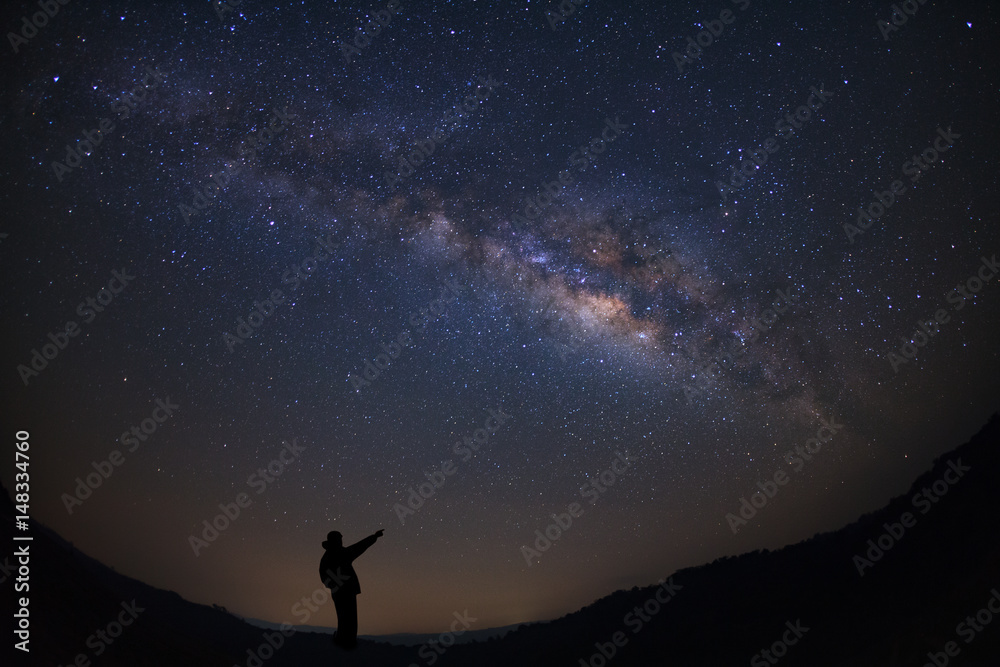 A Man is standing next to the milky way galaxy pointing on a bright star, Long exposure photograph, with grain.