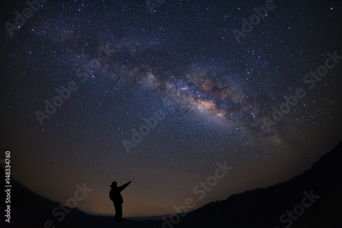 A Man is standing next to the milky way galaxy pointing on a bright star  Long exposure photograph  with grain.