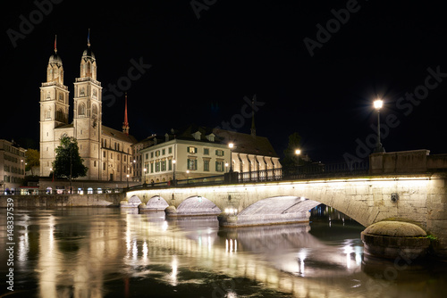 Nachtaufnahme Zürich mit beleuchteter Münsterbrücke und dem Grossmünster, mit Wasserspiegelungen in der Limmat