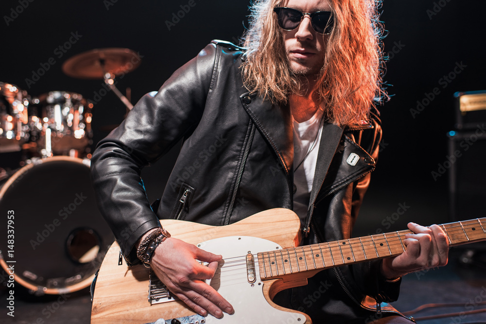 Fototapeta premium Handsome rock star in eyeglasses playing hard rock music with bass guitar on stage