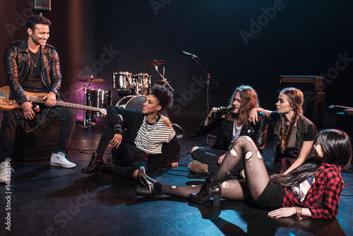 Young rock and roll band sitting together and drinking beer after concert on stage