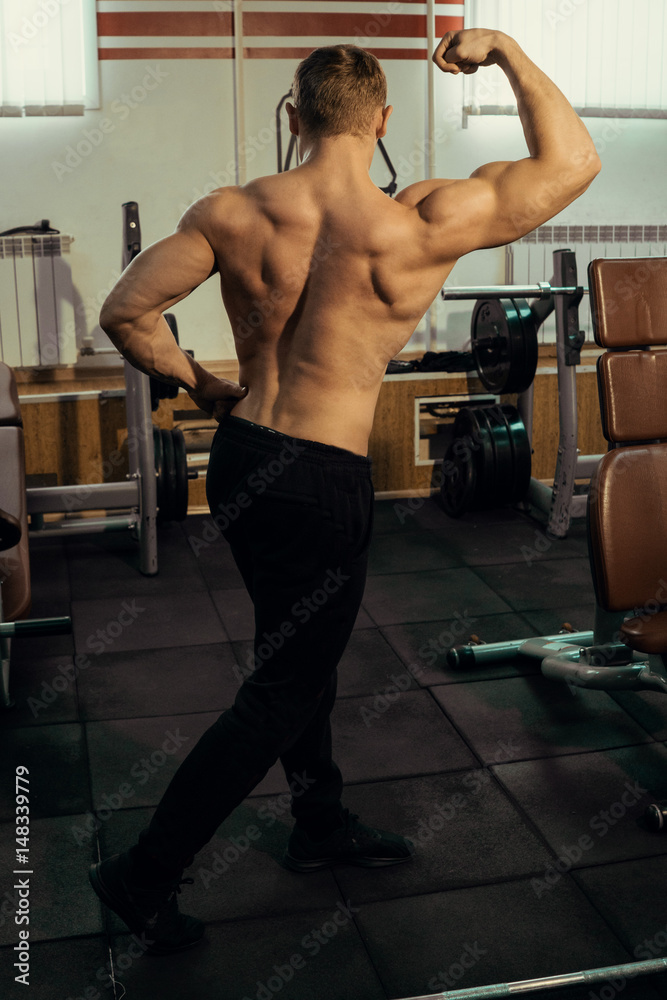 Naklejka premium Muscular athlete, bodybuilder with a naked torso posing in the gym. Hardened muscles, biceps